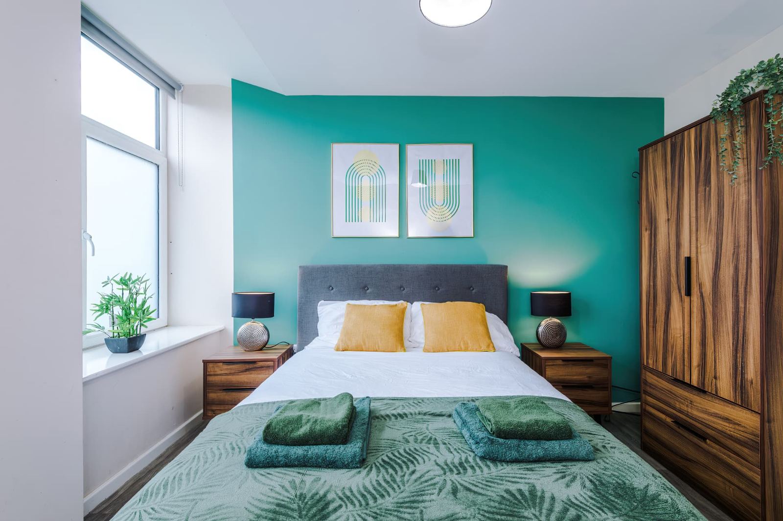 Double bedroom with a teal feature wall, bedside lamps and folded towels on the bed