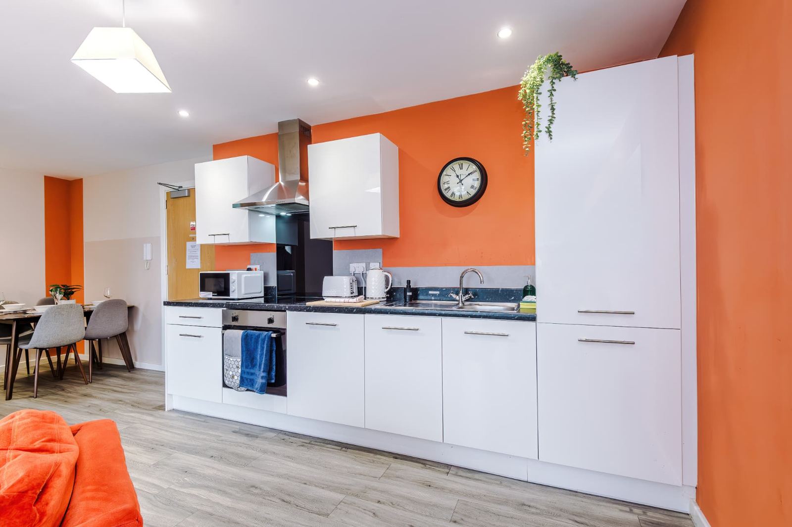 Fitted kitchen with an orange feature wall and a dining area in a furnished apartment